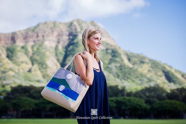 Woman in a blue dress caring a quilted tote bag with a Diamond Head design while standing in front of real-life Diamond Head.