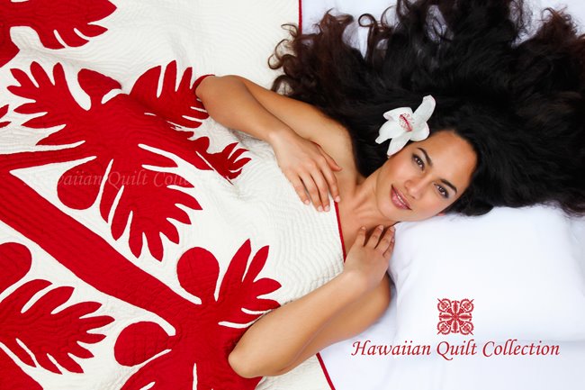 Brunette woman with a flower in her hair under a red & white Hawaiian quilt.