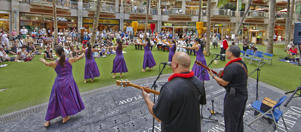 Hula troupe dancing for the crowd with a band performing in the background.