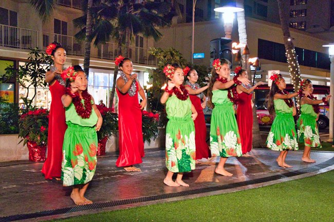 Group of hula dancers performing for an audience on the lawn in Waikiki.
