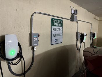 A parking area with multiple electric vehicle charging stations, illuminated with green lights, and a sign that reads "RESERVED PARKING ELECTRIC VEHICLES ONLY."