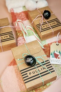 Small cardboard boxes with PULLIN logo wrapped in colorful string. A Christmas stocking & candy canes are also seen in the shot.