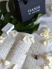 Gold necklace & white rose petals on a handwritten letter & an Oasis by Kolohe bag on the side.