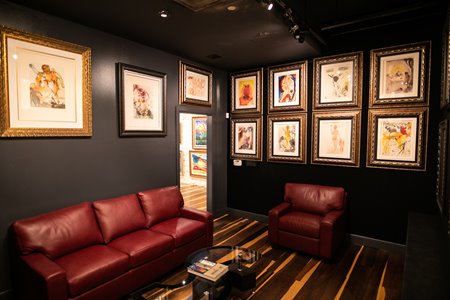 Multiple paintings hanging on black walls above red, leather sofas in a room at Park West Fine Art Museum & Gallery in Waikiki.