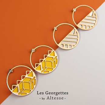 Two pairs of geometric gold hoop earrings side by side on an orange and grey split background.