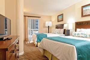 Bedroom of a suite at Club Wyndham at Waikiki Beach Walk featuring 2 beds, television, and door leading to the lanai/balcony.