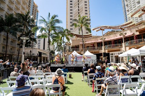a group of people sitting in chairs in a courtyard with palm trees watching a performance