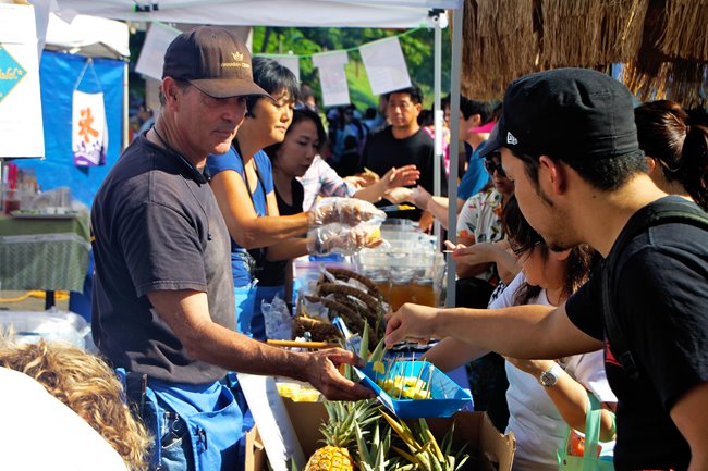 Local business owner offering samples of pineapple to customers at a farmers market in Waikiki