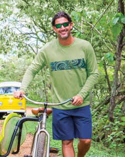Man wearing a green long sleeve while standing next to a bike in the forest