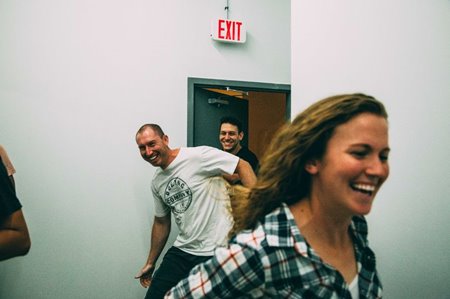 Smiling woman & 2 men running out of a door after successfully breaking out of an escape room at Breakout Waikiki.