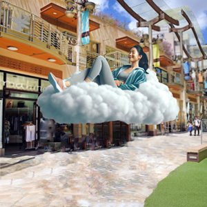 A woman with black hair and a blue jacket laying on a floating cloud in front of a 2-story open air mall strip