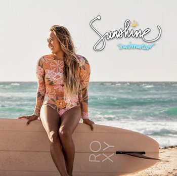 A woman wearing a bikini sits on a surfboard, soaking up the sun by the water.