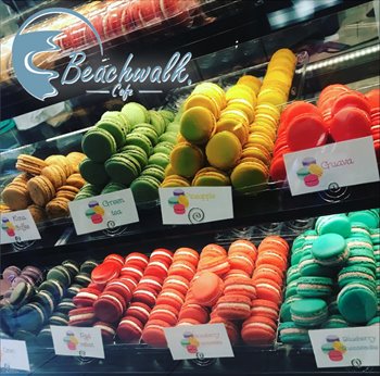 Different colored macaroons in a display case. Flavors shown are guava, pineapple, green tea, kona coffee, oreo, red velvet, strawberry cheesecake, and blueberry cheesecake