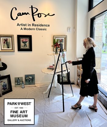 A woman painting a picture on an easel indoors, surrounded by furniture and a picture frame. The setting includes a modern art gallery with the text "Cam Pose," "Artist in Residence," "A Modern Classic," and "PARKTWEST EST. 1969 FINE ART MUSEUM GALLERY & AUCTIONS" visible on the wall. The woman is wearing casual clothing and footwear, using a tripod for support.