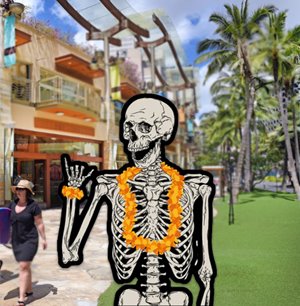 A skeleton wearing orange lei doing a shaka on its right hand. The background is of Waikiki Beach Walk store fronts.