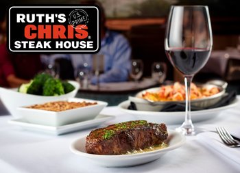 A table set in a restaurant featuring various plates of food, including meat dishes, accompanied by wine glasses and stemware. The table displays a menu or signage for Ruth's Chris Steak House.